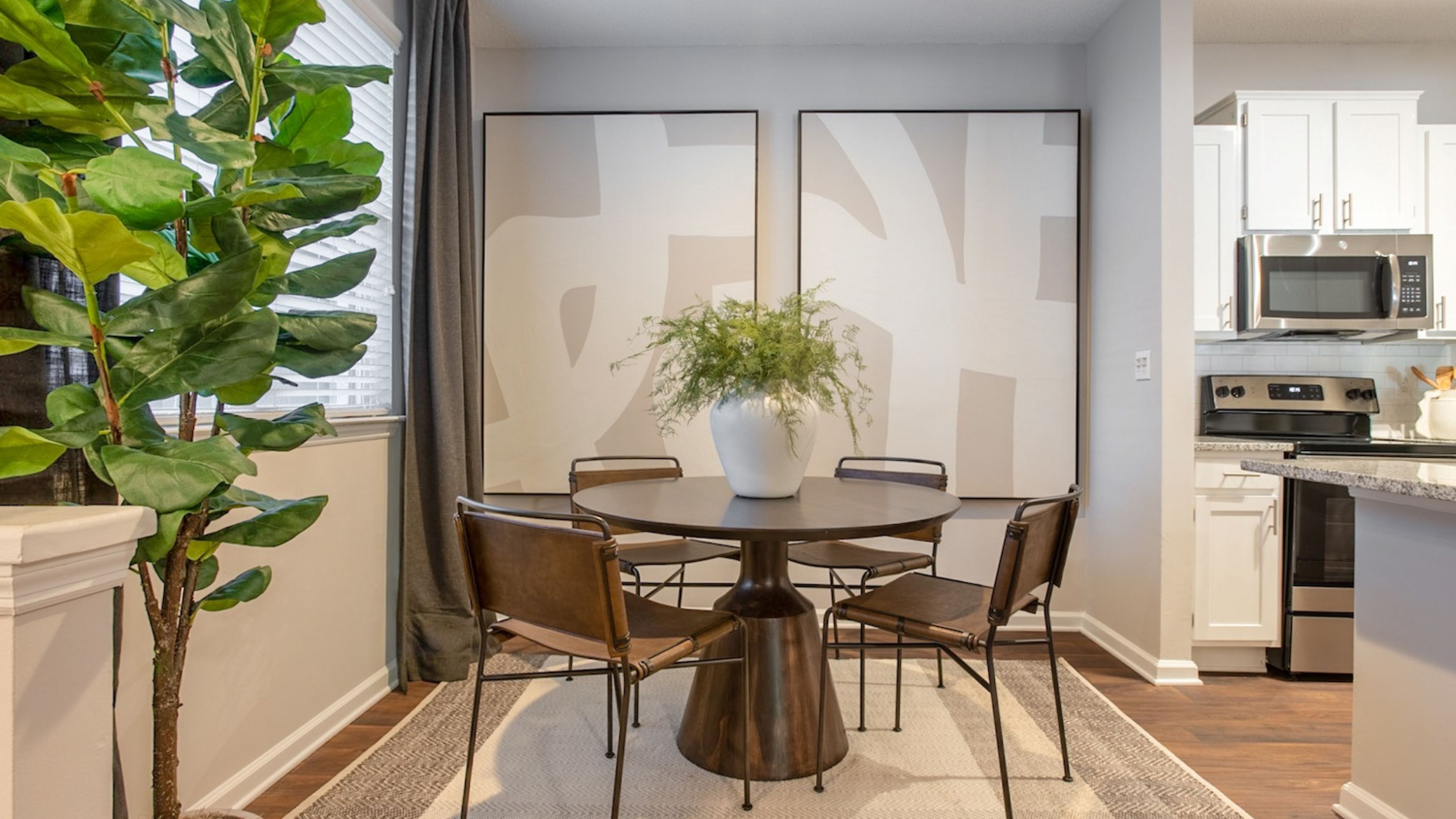 Hawthorne at the Parkway minimalist dining area with a round table and leather chairs, next to a modern kitchen and large leafy indoor plant.
